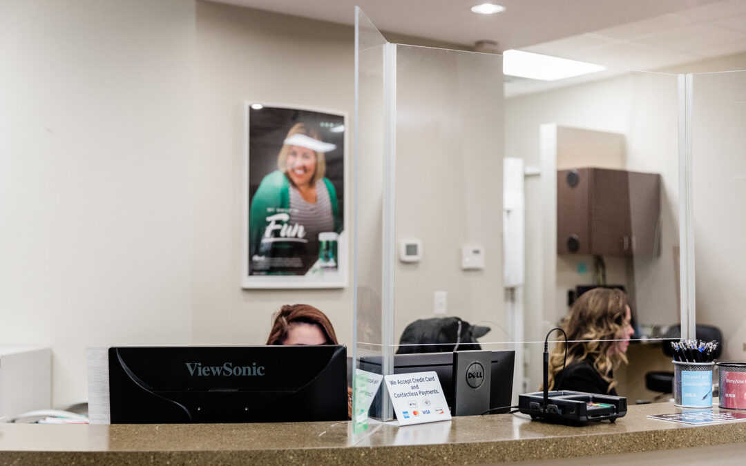 Reception desk at Hometown Dental Brannon Crossing with staff behind glass partition, featuring ViewSonic monitor and payment signage, showcasing a welcoming dental office environment.