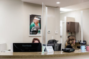 Reception desk at Hometown Dental Brannon Crossing with staff members, protective barriers, and a welcoming environment featuring a poster of a smiling woman.